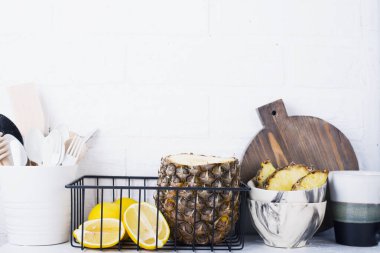 Mutfak raf beyaz arka plan, taze limonlar, ananas, mutfak aletleri, aletler, doğrama tahtaları, depolama sepetleri. Çevre dostu bir hayat. Ev tarzı, minimalizm, sağlıklı beslenme.