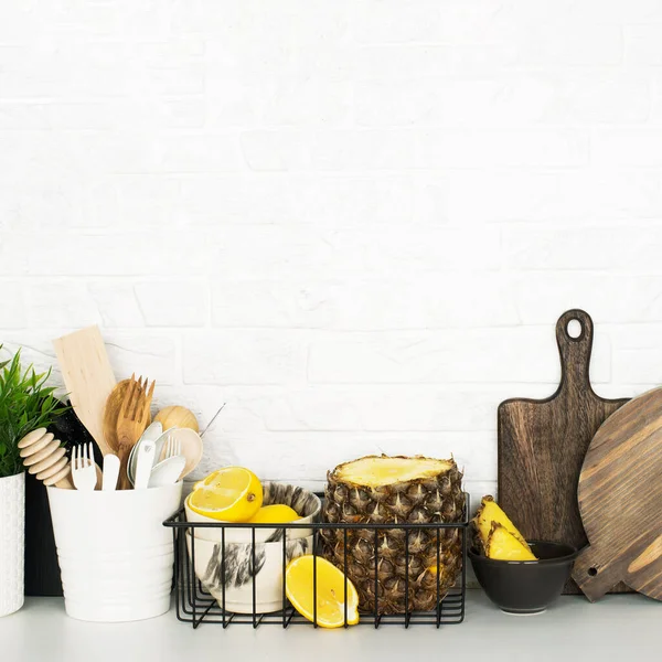 Kitchen shelf with baskets for storing products, pineapple, lemons, cutlery in a glass, chopping wooden boards on a white brick background. Style home scandi minimalism trend of modernity. Copy space — Stock Photo, Image