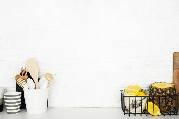 Kitchen shelf with baskets for storing products, pineapple, lemons, cutlery in a glass, chopping wooden boards on a white brick background. Style home scandi minimalism trend of modernity. Copy space — Stock Photo, Image