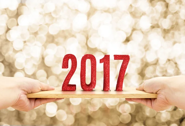 Placa de madeira mão segurando com 2017 feliz ano novo vermelho glitter num — Fotografia de Stock