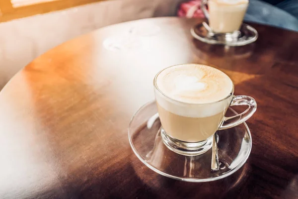 Latte coffee in clear cup on brown wood table top in cafe