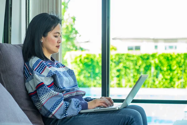 Lycklig kvinna sitter på bekväm soffa använder laptop nära fönster — Stockfoto