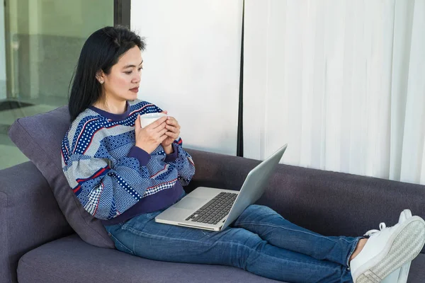 Donna felice con tazza di caffè caldo posa su comodo divano utilizzando — Foto Stock