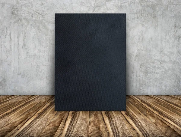 Blank black fabric canvas frame leaning at concrete wall on wood — Stock Photo, Image