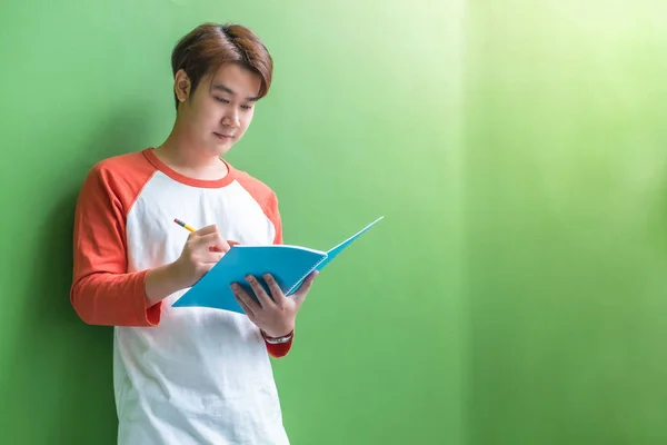 Молодий хлопчик-підліток пише на блакитному блокноті, спираючись на зелену прогулянку — стокове фото