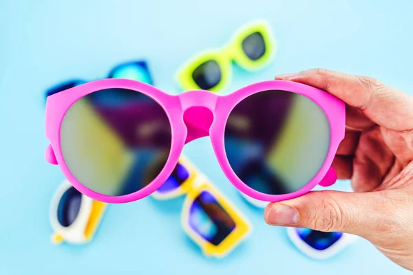 Hand som håller levande rosa solglasögon med oskärpa grupp av glasögon på — Stockfoto