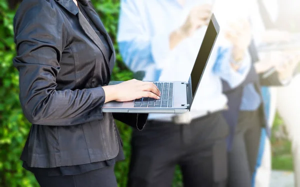 Business woman using laptop outside office with working team