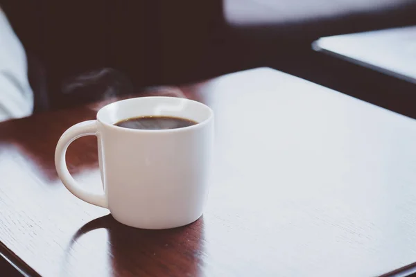 Kubek gorącej kawy czarny na drewniane blat w kawiarni z bliska — Zdjęcie stockowe