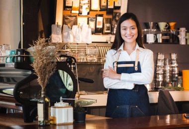 Asyalı kadın barista aşınma jean önlük sayaç, kollarını geçti