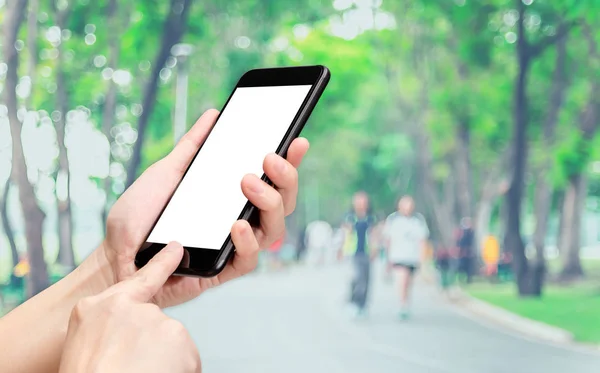 Haga clic en la mano del teléfono móvil con la gente borrosa ejercicio en el parque backgr —  Fotos de Stock