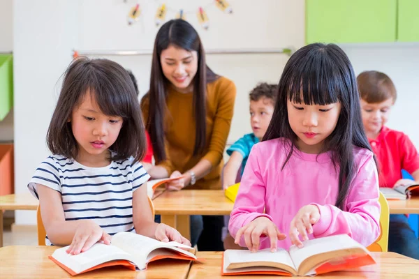 Två asiatiska flicka kid läsebok i klassrummet och medan lärare t — Stockfoto