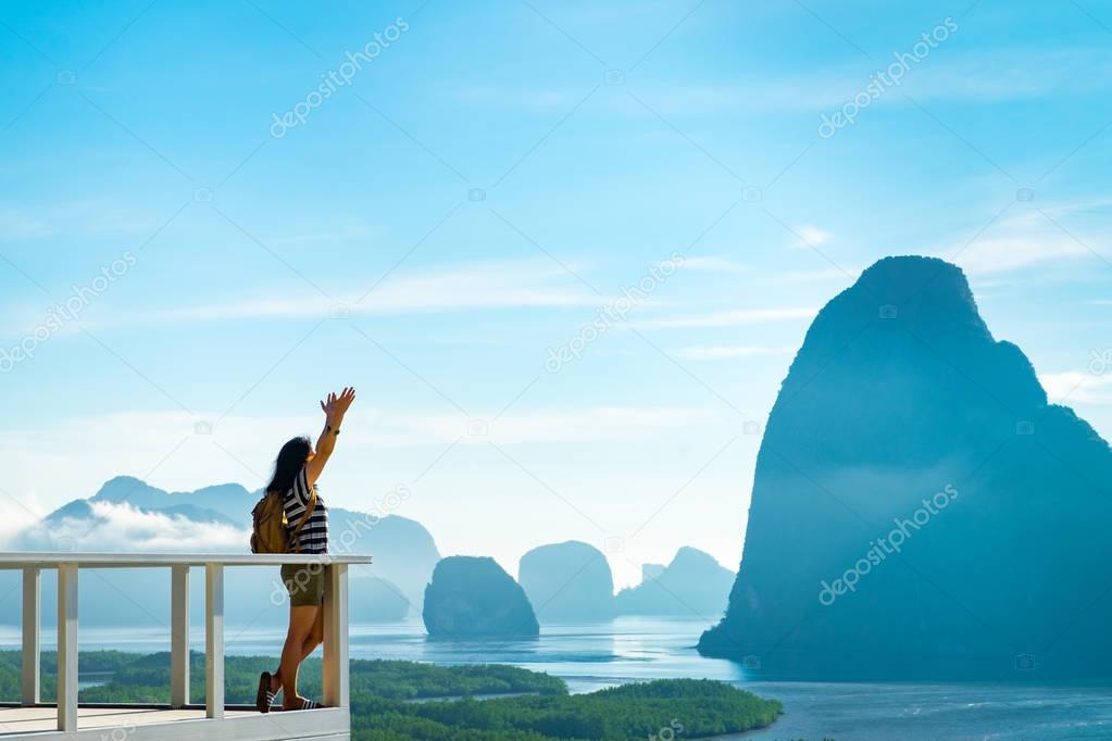 Happy young traveler woman backpacker raised arm up to sky enjoy