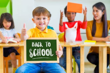 Çocuk çocuk başparmak yukarıya ve blackboard ile okul wor geri tutarak