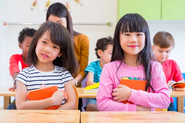 Two Asian girl kid hugging book and smiling in classroom and whi