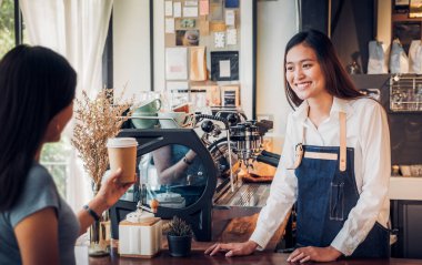 Asyalı kadın barista kahve kupasına gitmek hizmet jean önlük giymek 