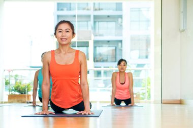 Stüdyo Oda, bir grup insan yukarı doğru köpek pozlar yaparken yoga sınıfında