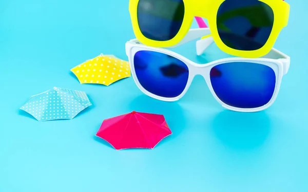 Gafas de sol de colores y sombrilla en el fondo del estudio azul claro , — Foto de Stock