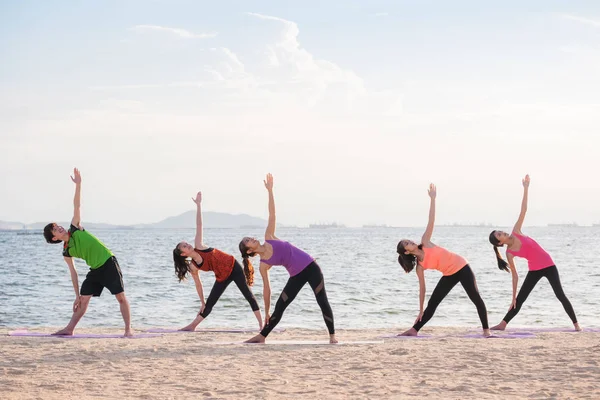Yoga sınıf deniz sahilinde akşam, bir grup insan Triang yapıyor