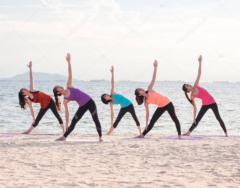 Yoga class at sea beach in evening ,Group of people doing Triang