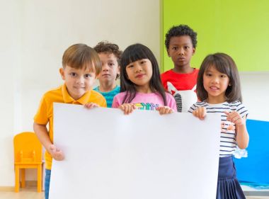 Kinderga, sınıfta boş poster tutan çeşitlilik çocuk