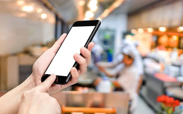Haga clic en la mano del teléfono móvil con blur chef en el fondo del restaurante —  Fotos de Stock