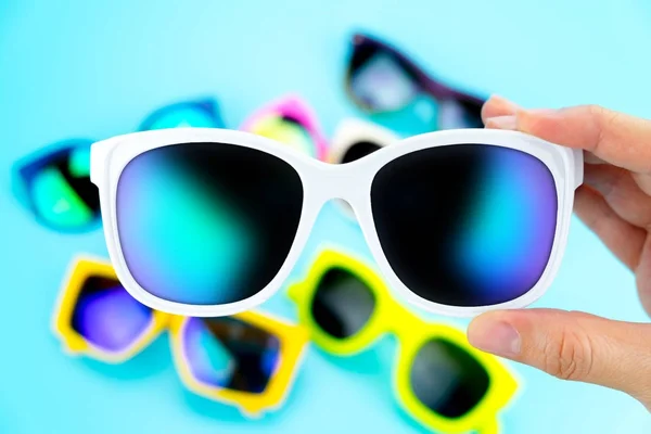 Mão segurando óculos de sol com grupo borrão de óculos no fundo — Fotografia de Stock