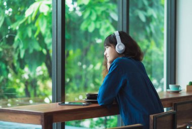 Mutlu Asyalı casual kadın yakınındaki kablosuz kulaklık ile müzik dinleme