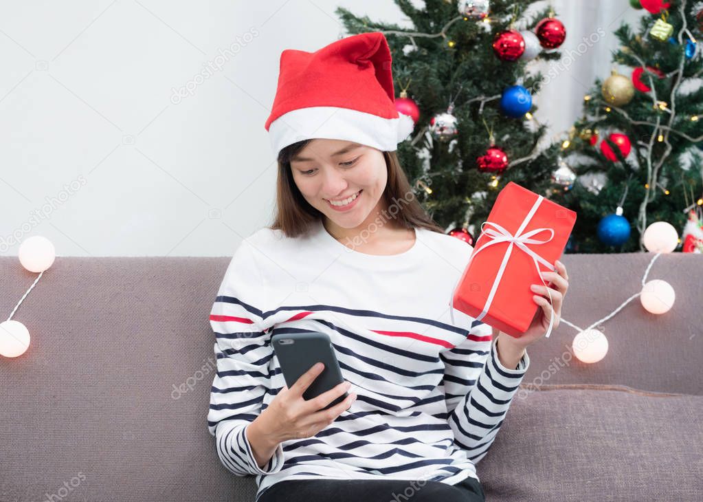 Asia woman wear santa hat and holding gift box and use mobile ch