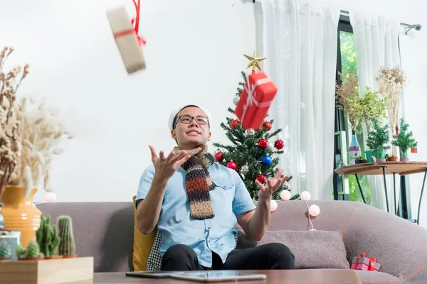 Asie homme porter santa chapeau assis sur canapé jeter deux boîte-cadeau rouge en ai — Photo