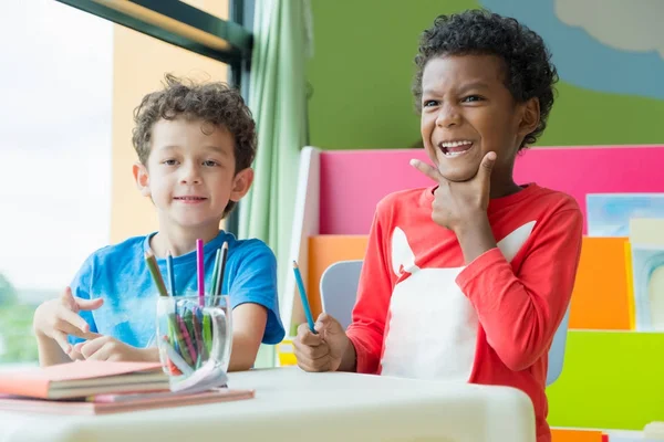 Двоє хлопчиків сидять на столі і розмальовують у книзі в дошкільній бібліотеці — стокове фото