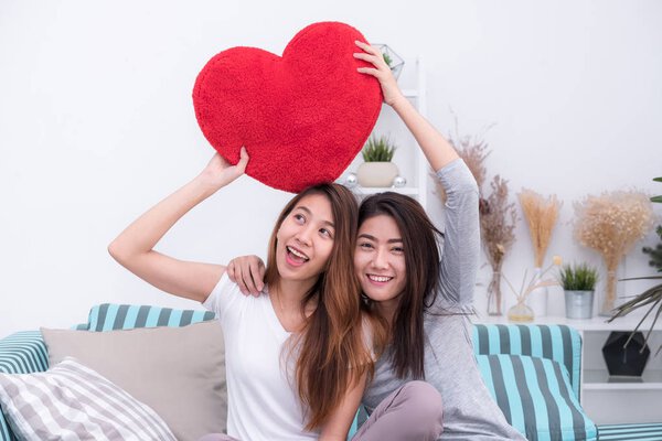 Asia lesbian lgbt couple holding red heart pillow together over 