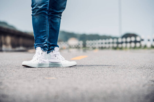 Close up woman wear jean and white sneaker standing on highway r