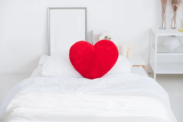 Close up red heart pillow lying on white bed in bedroom.Love val