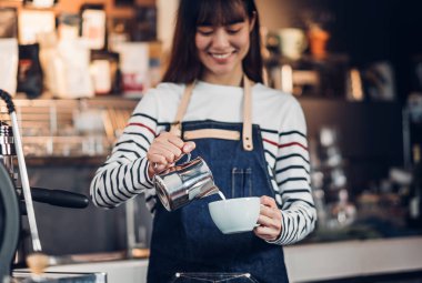Asya kadın barista sayaç barda sıcak kahve fincan içine süt dökün 