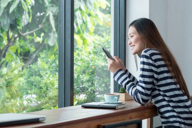 Caf pencerede yakınındaki mobil müzik dinleme kullanan mutlu Asya kadın