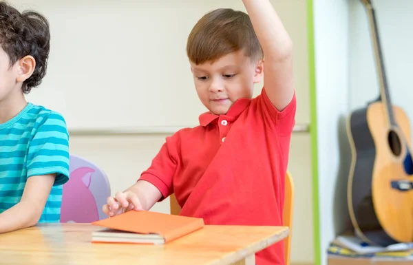 Дошкільна дитина піднімає руку, щоб відповісти на запитання вчителя на білому — стокове фото