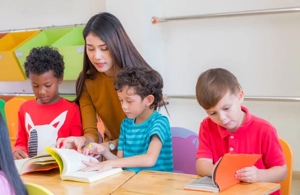 Asiática profesora enseñando diversidad niños leyendo libro en cla —  Fotos de Stock