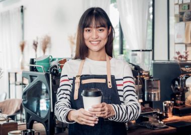 Asyalı kadın barista aşınma jean önlük sıcak tutan kahve götürün