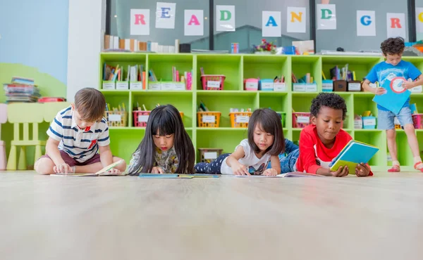 Grupo de niños de la diversidad tumbado en el suelo y leer el libro de cuentos i —  Fotos de Stock