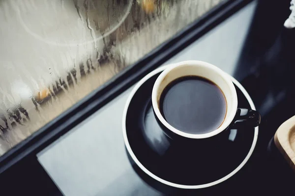 Taza de café negro en la mesa en el restaurante cafetería cerca de la ventana cuando ra — Foto de Stock
