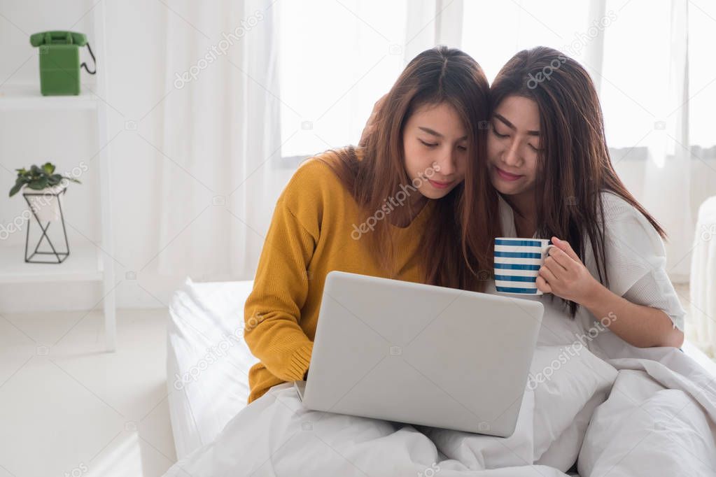 Asia lesbian lgbt couple sitting on bed hug and using laptop com