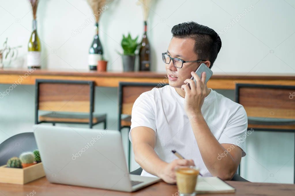 casual asian man talking on mobile phone working with laptop com