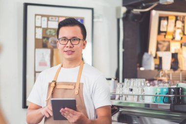 Asyalı erkek barista aşınma önlük tutun tablet bilgisayar kahve menü w