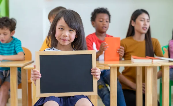 Kid girl holding blank blackboard with diversity friends and tea — Stock Photo, Image