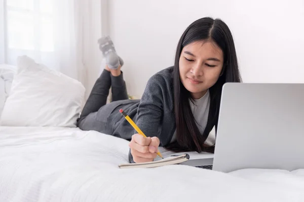 Asiatico donna posa su letto scrittura scartoffie su notebook mentre br — Foto Stock