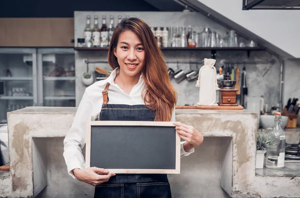 Asian female barista wear jean apron holding blank blackboard co