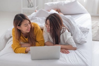 Asya lezbiyen lgbt çift kullanarak dizüstü bilgisayar beraber yatakta yatarken