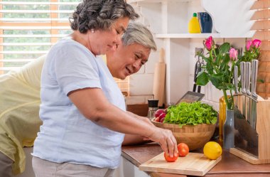 Asya kıdemli eşi ahşap kesme tahtası üzerinde domates dilimleme ve menü recipe.senior teknoloji lfiestyle.aging evde arama tablet bilgisayar kullanarak