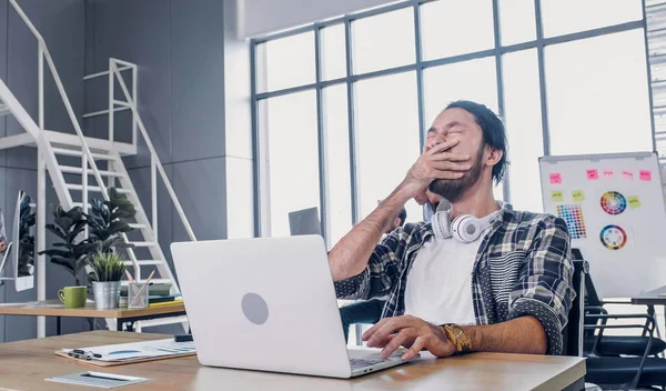 Творческий дизайнер зевает во время работы трудно и скучно с ноутбуком — стоковое фото
