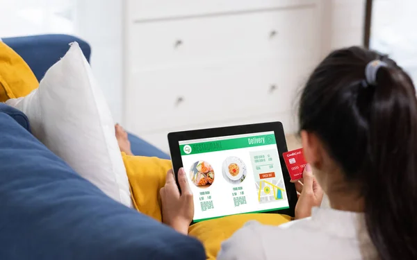 Азиатская женщина заказать еду онлайн с кредитной картой на планшете сидя — стоковое фото